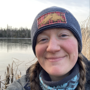 Corinne in front lake with blue hat and blue sweater 