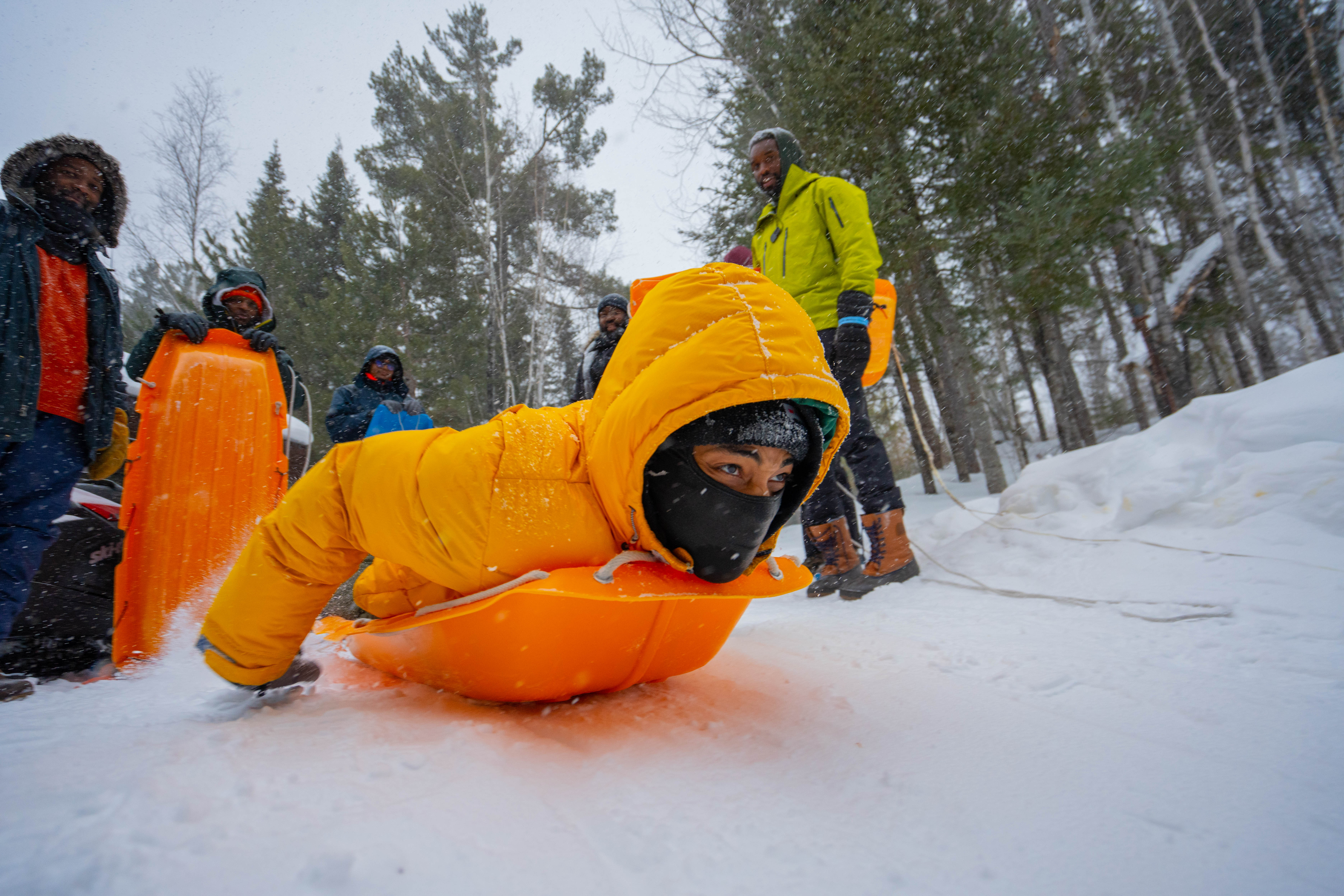 A participant of the Boyz N The Wood retreat sleds down a hill as others look on. (Photo credit: Dudley Edmondson)