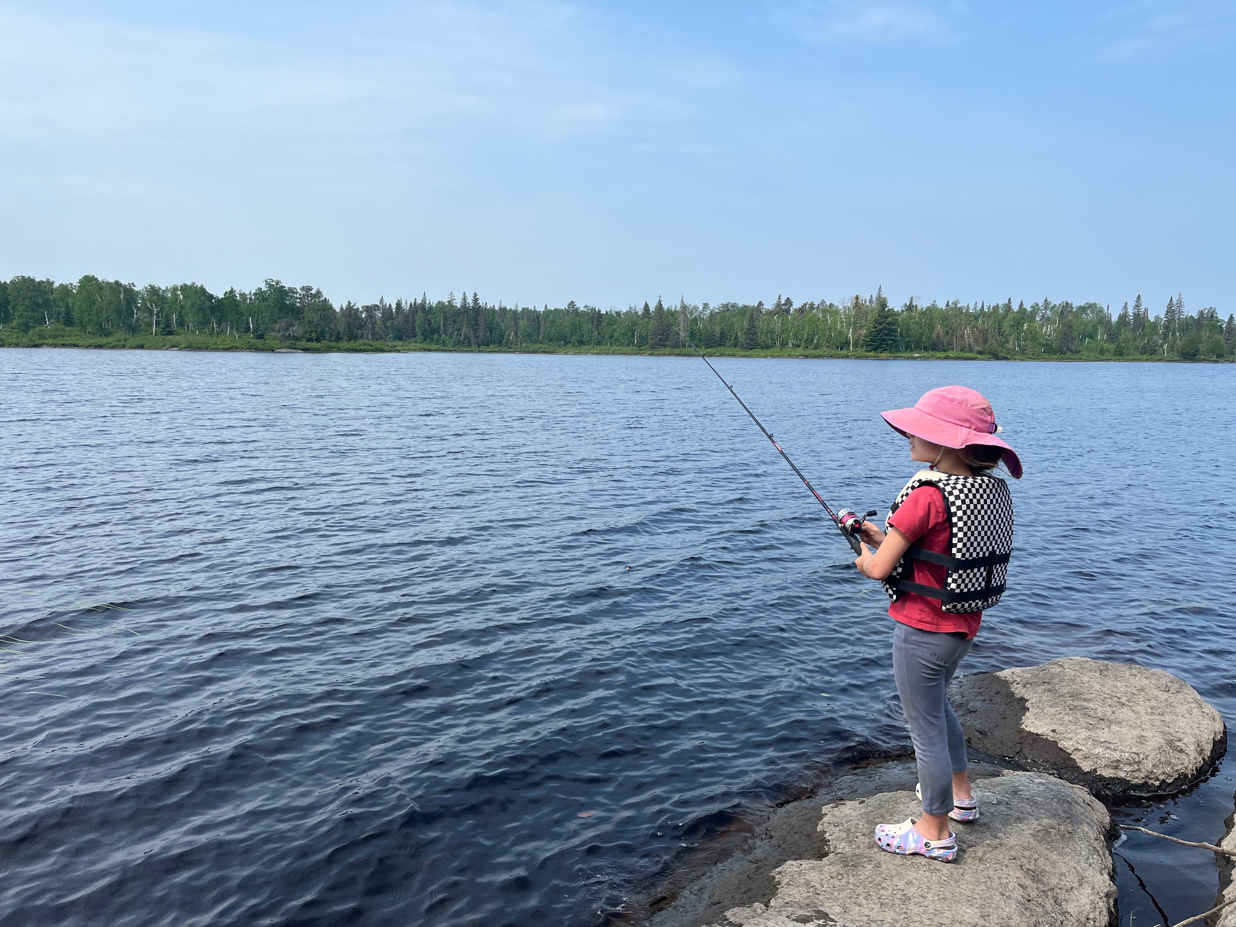 Kid fishing in Boundary Waters. Checkered life jacket. Fishing hat. 