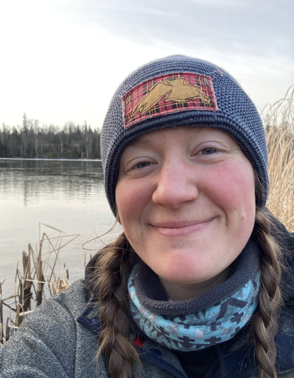 Corinne in front lake with blue hat and blue sweater 