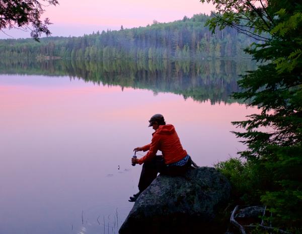 Woman sits on a rock looking out at a lake during a purple sunset