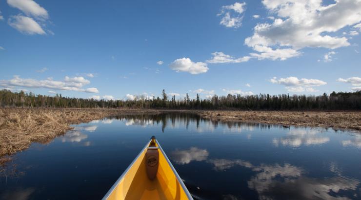 Photo of front of canoe on water with white clouds reflecting over Boundary Waters