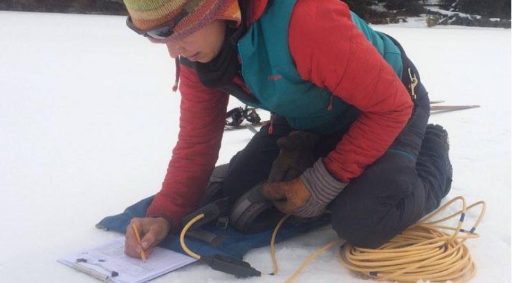 Photo of Amy Freeman kneeling on snow writing on clipboard