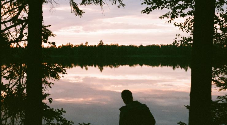 Image of person standing between two tree silhouettes looking out at pink boundary waters sunset