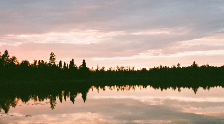 Photo of Boundary Waters sunset with light pink and blue sky and tree silhouettes on horizon