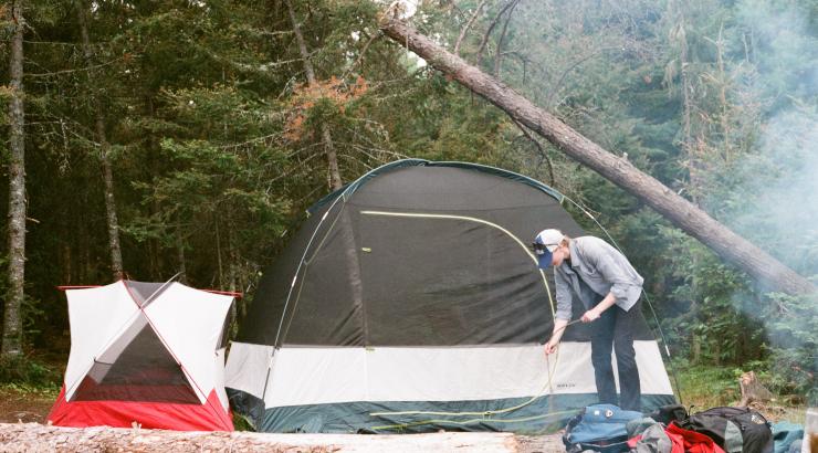 Photo of person picking up stick infront of two tents