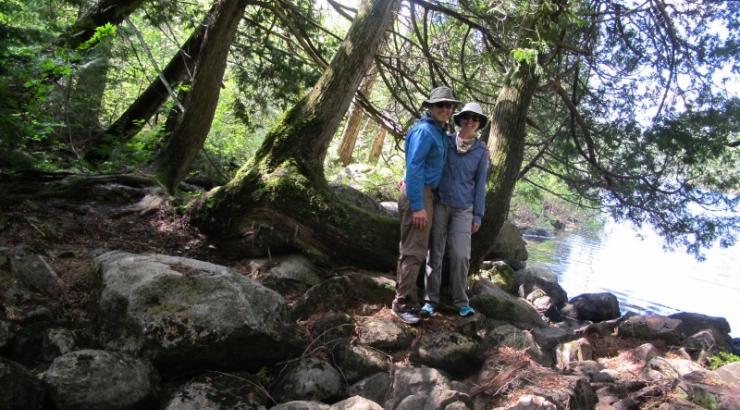 Photo of two people standing under trees on some rocks, smiling