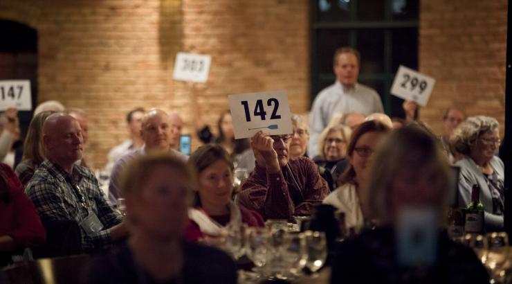 Photo of auction bidder sitting at table holding up sign with "142" on it