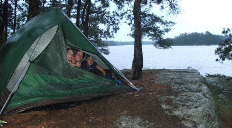 Photo of three boys peaking head out of green tent in Boundary Waters