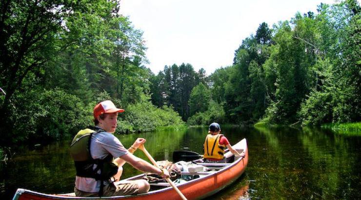 two teenagers paddling a red canoe