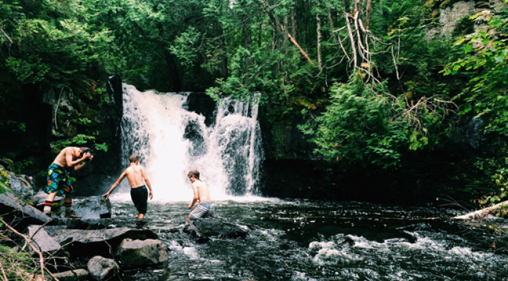 Photo of three youth standing in a waterfall in the Boundary Waters