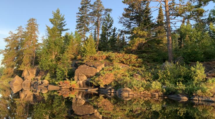 photo of clif-like rocks and trees reflecting onto still water