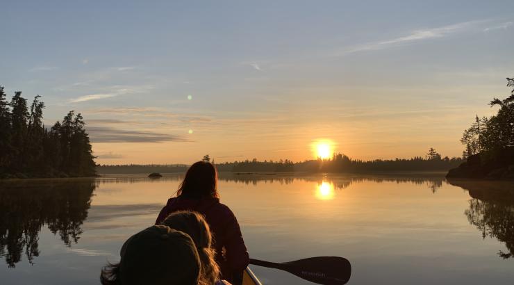 image of backs of three people paddling into the sunrise with sun on the horizon