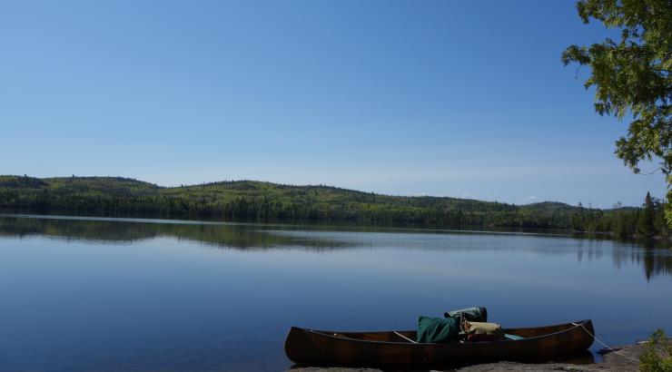 Photo of canoe on shore infront of bright blue sky reflecting on water