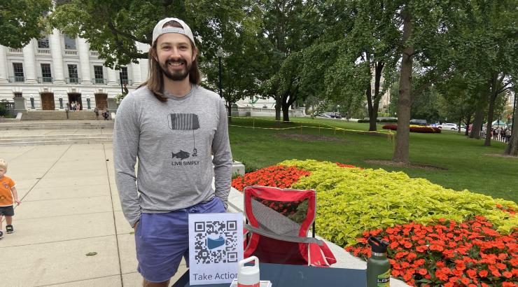 A photo of Dylan Duerre, the Madison ambassador for the Campaign to Save the Boundary Waters, posing in front of the table he operates at the Madison Farmers Market.
