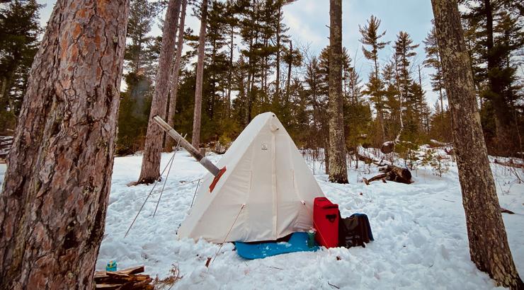 A canvas hot tent sits in the snowy woods.