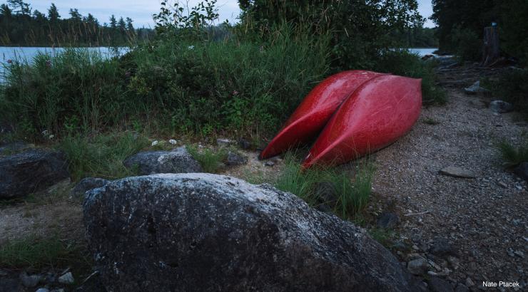 Two red canoes sit upside near a campsite in the Boundary Waters (Photo Credit: Nate Ptacek)
