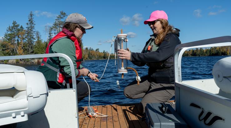 Two researchers handle water quality testing eqipment near a lake. 