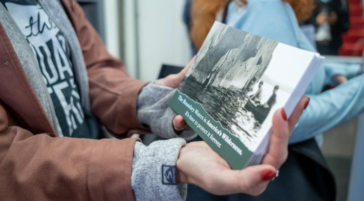 A close-up photo of someone holding a stack of green postcards that read "The Boundary Waters is America's Wilderness"