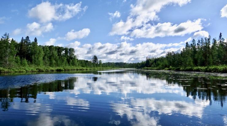 Image of blue sky with white fluffy clouds reflecting onto still water in Boundary Waters