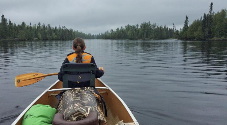 Photo of the back of a youth at the front of a canoe, paddling