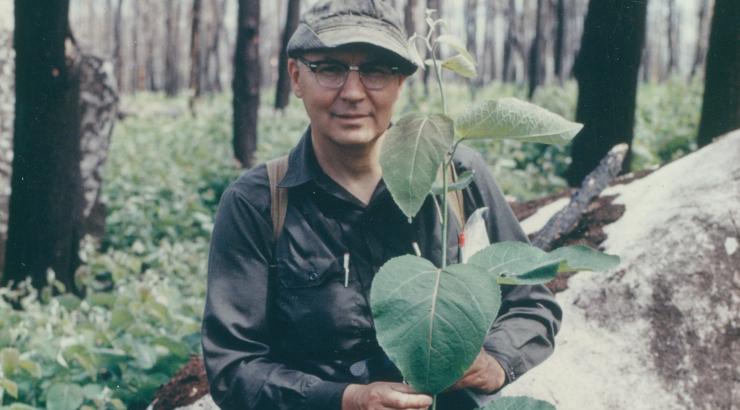 Bud Heinselman wearing glasses and a cap holding a leaf