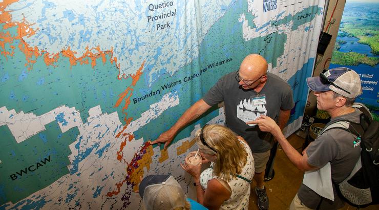 Photo of 3 people around ED Tom Landwehr pointing at BWCA map on wall