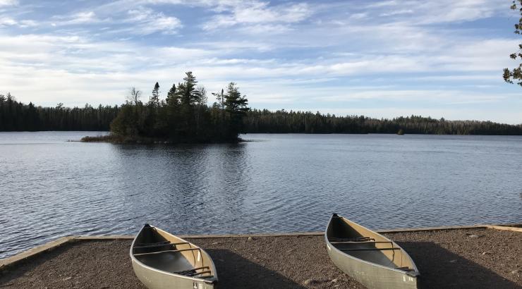 Photo of 2 canoes sitting next to eachother on the shore of a lake