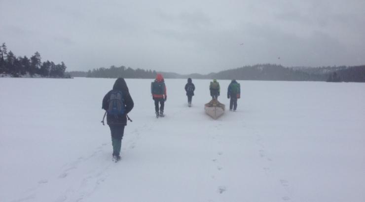 Photo of 5 people walking on snow covered Boundary Waters lake pulling canoe behind them