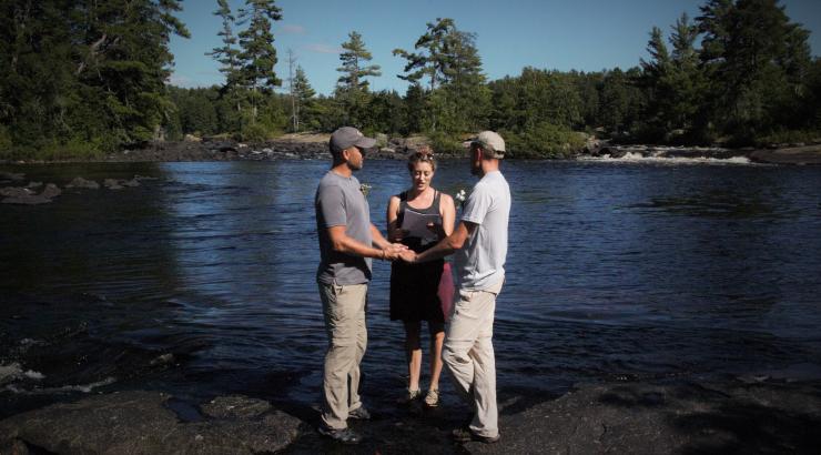 Photo of 2 men holding hands getting married infront of a woman in the Boundary Waters