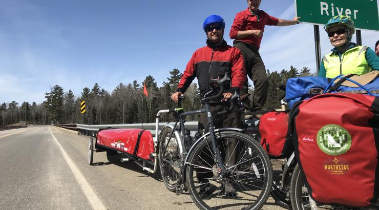 photo of 3 people standing next to 2 bikes with Northstar Canoe packs strapped on them, and a red canoe in the back attached to the bike