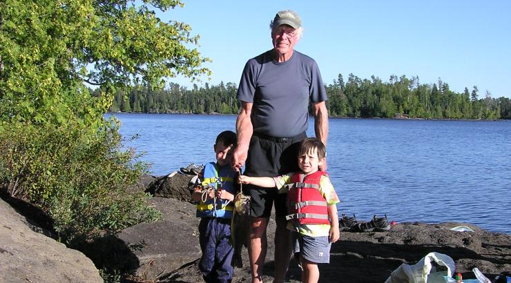 Picture of older man standing between two young kids on shore of the Boundary Waters