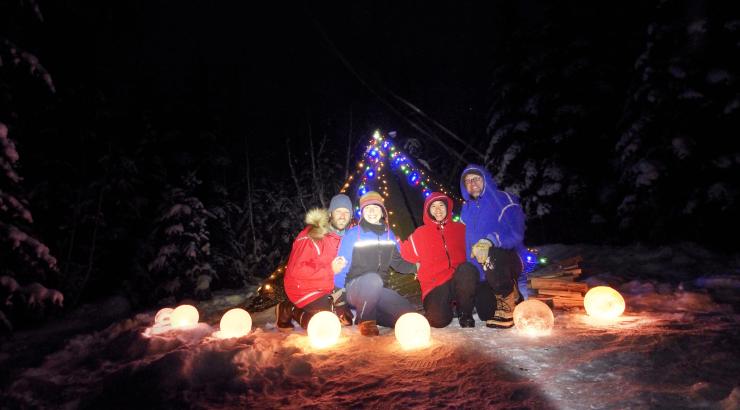 5 people sitting around luminaries infront of a tent with lights strung on it 
