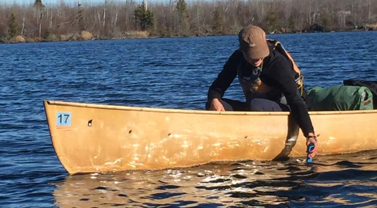 Amy Freeman reaching over side of canoe to accept water quality sample