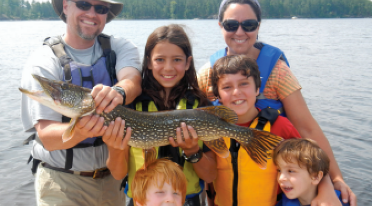 6 people standing next to a lake holding a big fish 