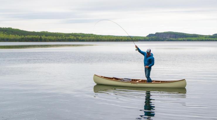 photo of man standing up fishing in a Merrimack Canoe