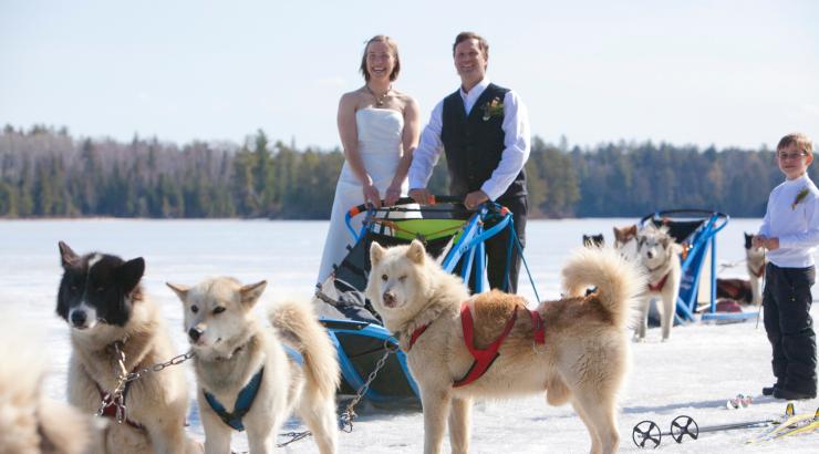 Photo of Dave and Amy freeman in wedding attire standing on sled with sled dogs