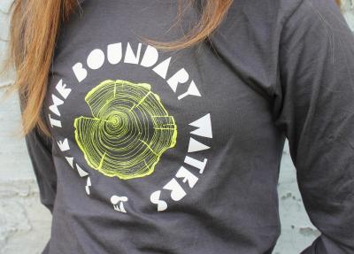 Photo of grey long sleeve shirt with Save the Boundary Waters printed in a circle around the image of a tree stump in yellow