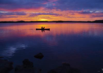Sunset over a lake with a silhouetted paddler and their dog in a canoe