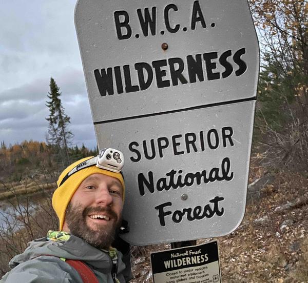 Alex Falconer poses next to a BWCAW entry sign on the first run of his trail-run traversal of the Boundary Waters.