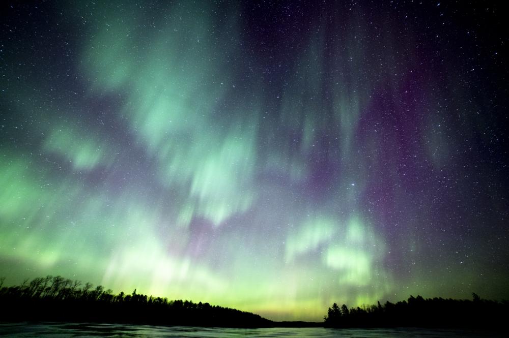 The northern lights shine in blue, green, and purple over a Boundary Waters lake