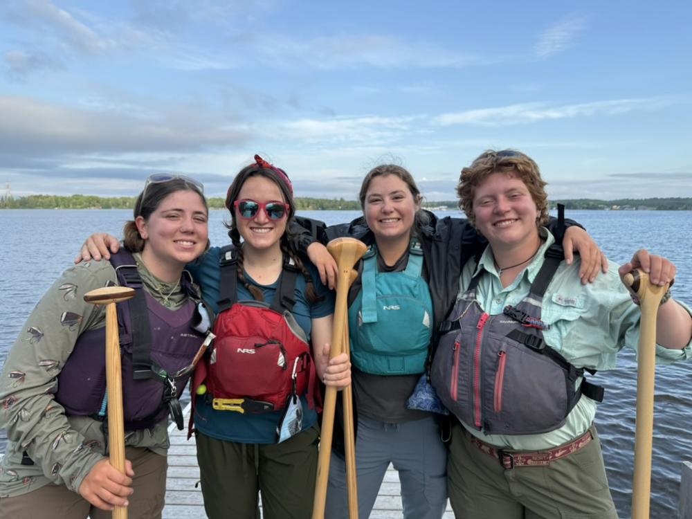 Hudson Bay Girls crew members stand together near a lake celebrating their accomplishment.