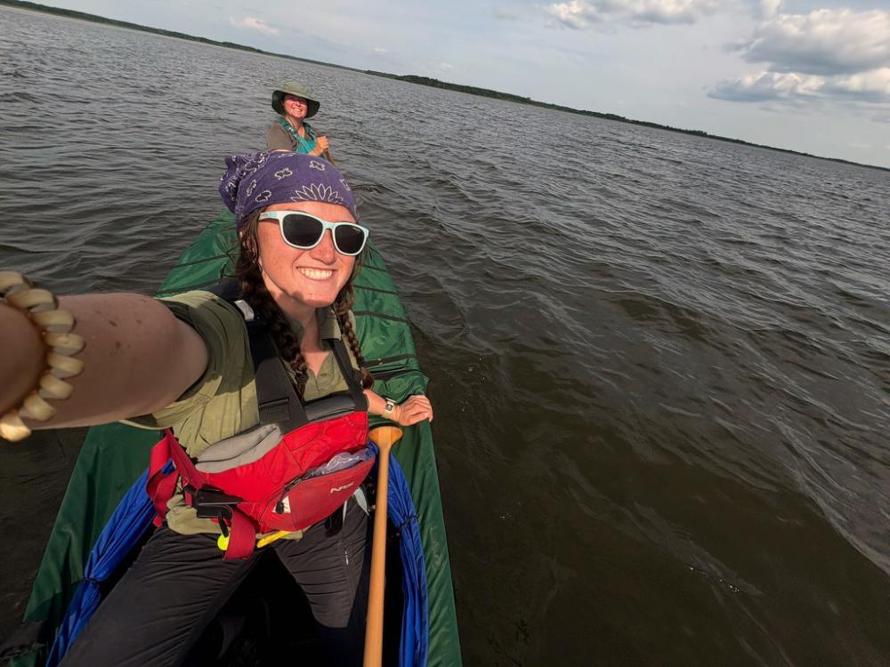 Two crew members of the Hudson Bay Girls paddle a canoe across a large lake.