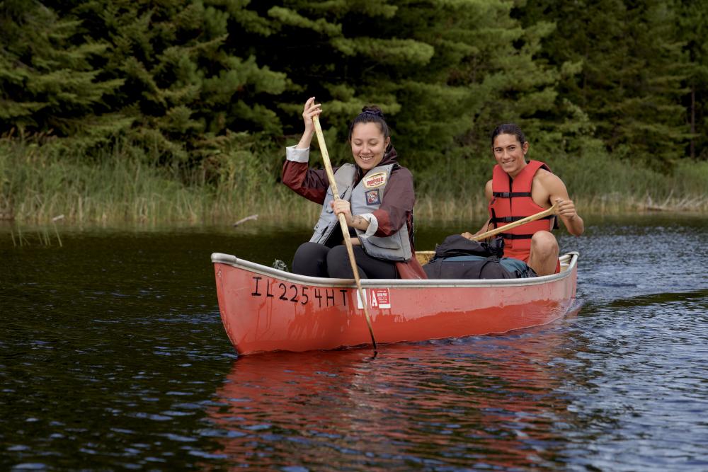 Two people smile as they steer a red canoe in the Boundary Waters