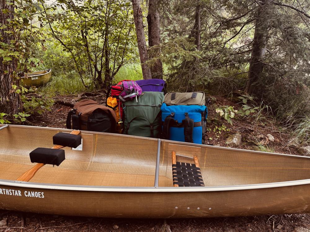 One canoe and multiple, colorful canoe packs sit together at a portage trail. 