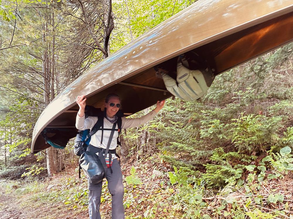 A woman portages a kevlar canoe down a wilderness trail. 