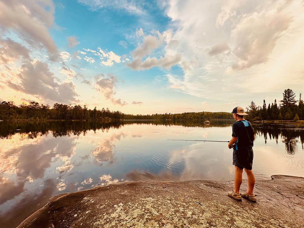 A teenage boy fishes on a calm evening near the shore. 