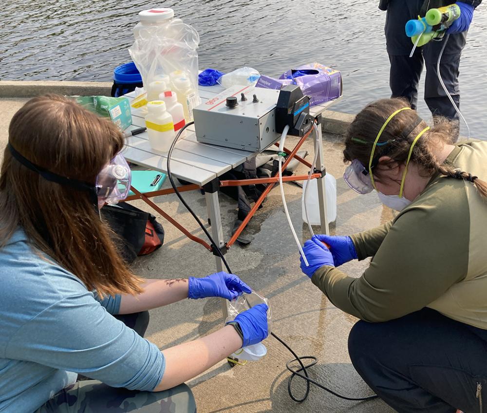 Three researchers work with water sampling equipment next to a lake.