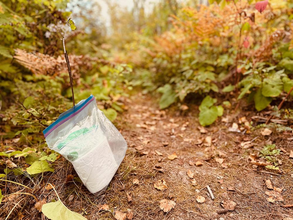 A bag of toilet paper and hand sanitizer sits near the latrine trail.