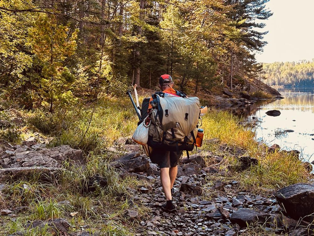 A man carrys a canoe pack and paddles down a portage trail. 